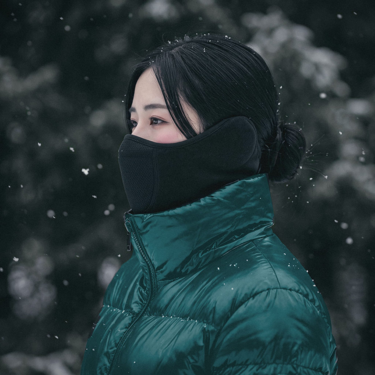 Side profile of a woman in a teal puffer jacket wearing the Face Guard in the snow